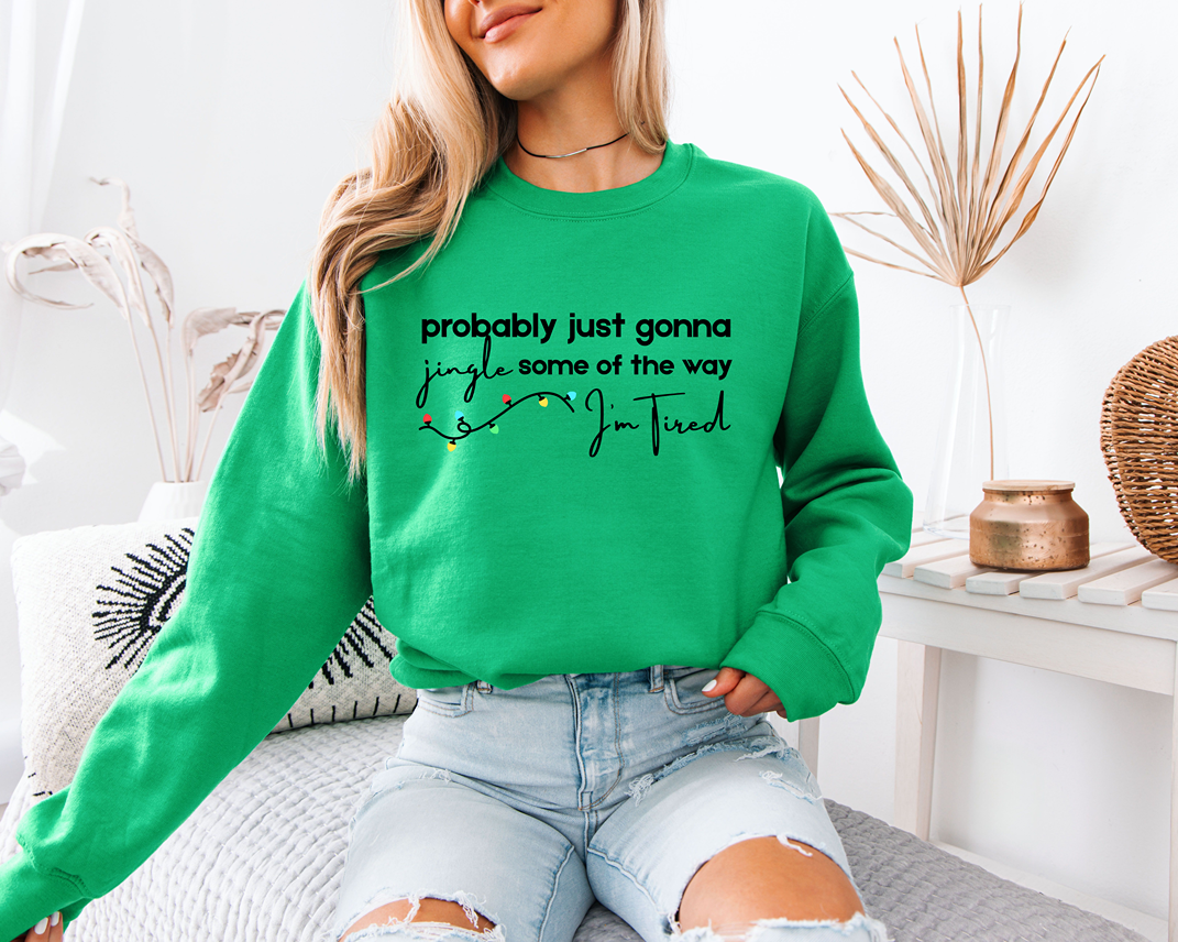 woman wearing a kelly green christmas sweatshirt that says probably gonna jingle some of the way im tired with christmas lights